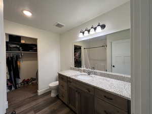 Primary Full Master Suite bathroom with visible vents, vanity, wood finished floors, toilet, and a walk in closet