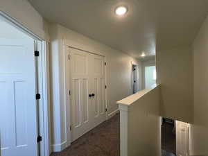 Hallway featuring dark carpet, recessed lighting, baseboards, and an upstairs landing