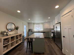 Kitchen with stainless steel appliances, light stone counters, dark wood finished floors, and a center island