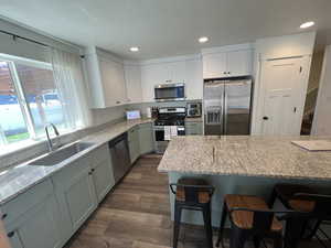 Kitchen with dark wood-style flooring, a breakfast bar, light stone countertops, a sink, and appliances with stainless steel finishes