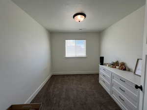 Unfurnished room featuring a textured ceiling, baseboards, visible vents, and dark carpet