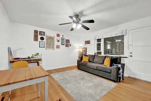 Living area featuring light wood-style floors, baseboards, a ceiling fan, and a textured ceiling