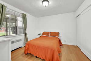 Bedroom with radiator, baseboards, a textured ceiling, and wood finished floors