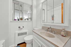 Bathroom with radiator heating unit, vanity, toilet, and wood finished floors
