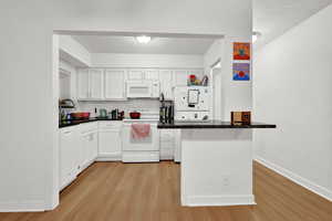 Kitchen with light wood-type flooring, a sink, white cabinets, and white appliances