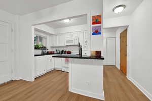 Kitchen featuring light wood finished floors, white appliances, white cabinetry, a peninsula, and backsplash