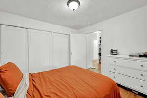 Bedroom with light wood-style flooring, two closets, and a textured ceiling