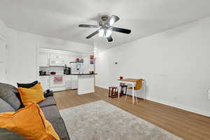 Living room with a textured ceiling, ceiling fan, baseboards, and light wood-style floors