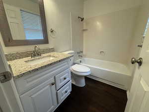 Bathroom with toilet, washtub / shower combination, wood finished floors, and vanity