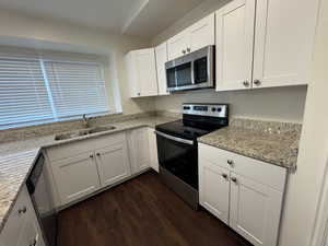 Kitchen with dark wood finished floors, a sink, light stone counters, stainless steel appliances, and white cabinetry