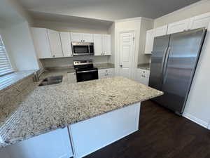 Kitchen with light stone counters, a sink, a peninsula, and stainless steel appliances