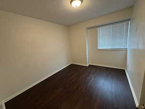 Spare room with baseboards, dark wood-style flooring, a textured ceiling, and visible vents