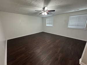 Unfurnished room featuring a textured ceiling, a ceiling fan, baseboards, dark wood-type flooring, and visible vents