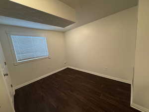 Empty room with baseboards, a textured ceiling, and dark wood-style flooring