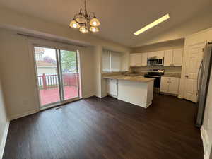 Kitchen with visible vents, appliances with stainless steel finishes, a peninsula, a chandelier, and dark wood-type flooring