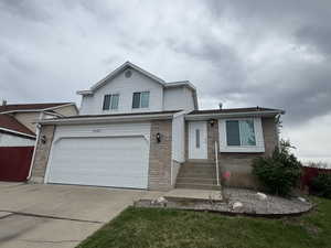 Tri-level home with brick siding, a garage, fence, and concrete driveway