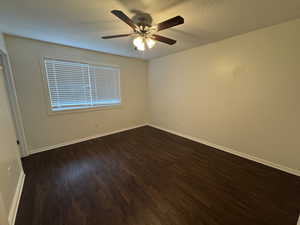 Spare room with baseboards, a ceiling fan, a textured ceiling, and dark wood-type flooring