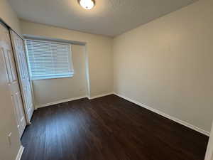 Unfurnished bedroom featuring a textured ceiling, visible vents, baseboards, a closet, and dark wood-type flooring