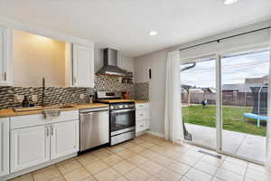 Kitchen featuring wall chimney range hood, decorative backsplash, appliances with stainless steel finishes, a sink, and butcher block counters