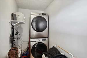 Washroom with laundry area, stacked washer and dryer, and a textured ceiling