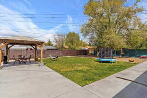 View of yard with a trampoline, a patio area, a gazebo, a fenced backyard, and a playground