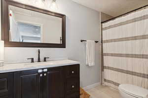 Full bathroom featuring vanity, toilet, a textured ceiling, a shower with shower curtain, and baseboards