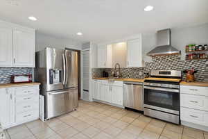 Kitchen featuring a sink, butcher block countertops, stainless steel appliances, and wall chimney exhaust hood