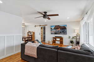 Living area with light wood-style floors, ceiling fan, recessed lighting, and a barn door