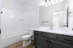 Bathroom featuring toilet,  shower combination, wood finished floors, and vanity