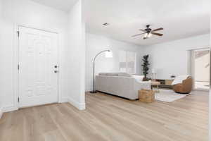 Living room with light wood-style floors, baseboards, a ceiling fan, and visible vents