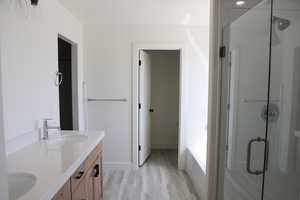Full bath with wood finished floors, a sink, a stall shower, and double vanity