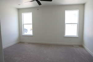 Carpeted empty room with ceiling fan, visible vents, and baseboards