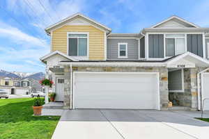 View of front of property featuring board and batten siding, an attached garage, driveway, and stone siding