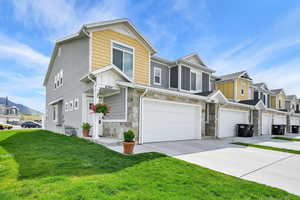 View of property with driveway, a front yard, a residential view, an attached garage, and stone siding
