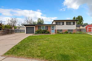 Tri-level home featuring a garage, a front lawn, fence, brick siding, and concrete driveway