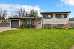 Tri-level home featuring fence, brick siding, a garage, a front yard, and driveway