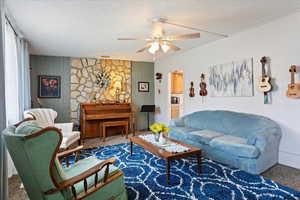 Living room featuring carpet floors, ceiling fan, visible vents, and wood walls
