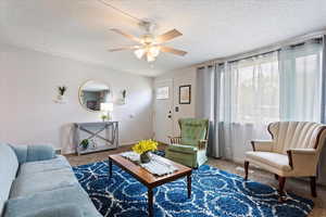 Carpeted living room with a ceiling fan, a textured ceiling, and baseboards