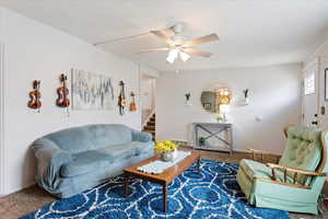 Carpeted living room featuring a textured ceiling, a ceiling fan, baseboards, visible vents, and stairway