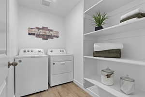 Laundry area with laundry area, washing machine and dryer, light wood-style flooring, and visible vents