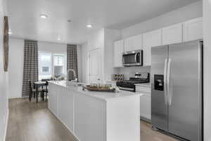 Kitchen with appliances with stainless steel finishes, a sink, light wood finished floors, a kitchen island with sink, and white cabinetry