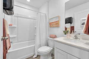 Bathroom with vanity, wood finished floors, shower / bath combination with curtain, and toilet
