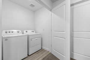 Clothes washing area featuring washer and dryer, laundry area, light wood finished floors, baseboards, and visible vents