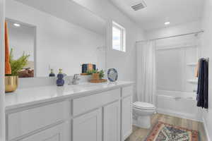 Bathroom featuring shower / bath combination with curtain, visible vents, wood finished floors, vanity, and toilet