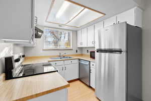 Kitchen with light countertops, stainless steel appliances, light wood-type flooring, white cabinets, and exhaust hood