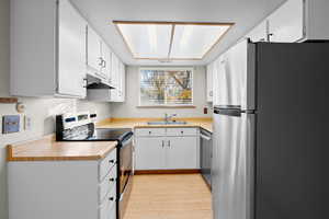 Kitchen featuring appliances with stainless steel finishes, light countertops, light wood-style flooring, and white cabinets