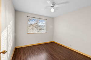 Unfurnished room featuring dark wood-style flooring and a ceiling fan
