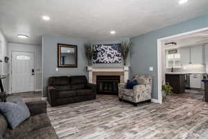 Living room with LVP floors, a fireplace, baseboards, recessed lighting, and a textured ceiling