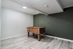 Recreation room featuring beamed ceiling, baseboards, and light wood-style floors