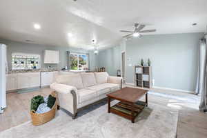 Living room with a textured ceiling, light wood-style flooring, ceiling fan, and a wealth of natural light